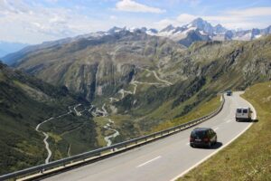 Wohnmobil auf kurvenreicher Alpenstraße vor verschneiten Berggipfeln