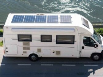 Wohnmobil mit mehreren Solarpaneelen auf dem Dach neben einem Gewässer